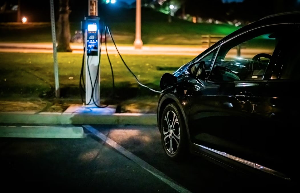 Black Electric Vehicle connected via cable to charge station at night
